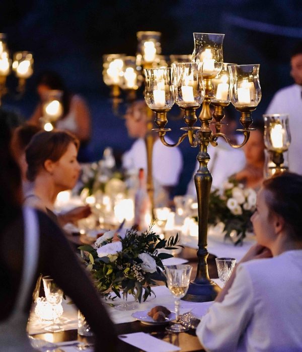 Decorated tables with floral composition and old fashioned candlesticks and guests in the celebration evening